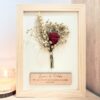 Cuadro de madera con rosa eterna preservada roja y flores secas, placa personalizada grabada con nombres y frase romántica, fondo blanco verjurado