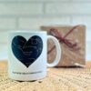 Taza blanca personalizada con mapa estelar en forma de corazón y texto 'Bajo este cielo comenzó todo', junto a caja de regalo con lazo