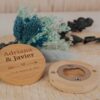 Abrebotellas de bambú personalizado para boda con nombres Adriana y Javier y fecha grabados, junto a flores secas azules sobre fondo de madera natural