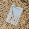 Llavero personalizado madera con inicial M y nombre grabado, cordón de ante verde sobre tarjeta agradecimiento boda