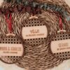Tres bolas de Navidad de madera con diseño ratán calado y frases personalizadas grabadas: 'Vega mi primera Navidad', 'Amaya & Ignacio recién casados' y 'Gerard te quiero 4x4', sobre fondo natural con decoración navideña
