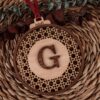 Bola de Navidad personalizada de madera ratán con inicial G grabada, patrón geométrico y cinta roja sobre fondo natural