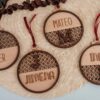Cuatro bolas de Navidad personalizadas en madera de arce con diseño ratán y nombres grabados (Iker, Jimena, Mateo, India) con cinta roja sobre fondo de rafia natural