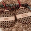 Dos bolas de Navidad personalizadas con nombres Iker y Susana en madera de arce con diseño ratán, cinta roja y eucalipto seco sobre cesta artesanal