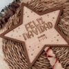 Estrella de Navidad personalizada en madera con grabado Feliz Navidad, versión ratán con calados decorativos y ribete nogal, sobre fondo natural con eucalipto seco