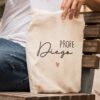 Totebag de algodón natural personalizada con nombre Diego y texto Profe grabado a láser, sostenida por persona sentada en banco de madera