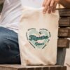 Tote bag de algodón beige personalizada para profesores con diseño retro corazón verde menta y nombre Oliver grabado, sujetada por una persona sentada
