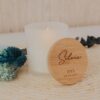 Vela aromática blanca con tapa de bambú personalizada grabada con nombre Silvia, iniciales A♡L y fecha de boda, sobre mantel de ratán con flores secas azules