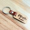 Llavero de madera personalizado con letra infantil PAPÁ te quiero grabado a láser, con cuero marrón y anilla metálica sobre mesa de madera